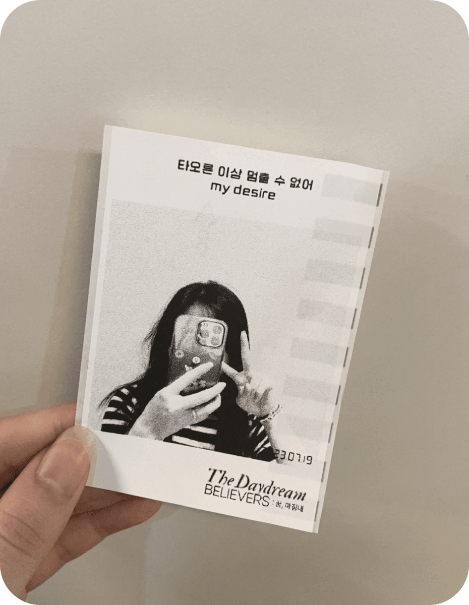 흑백 인물 사진 위에 가사 한 구절, 아래에 The Daydream Believers 로고가 인쇄된 영수증사진기® 출력물을 든 손